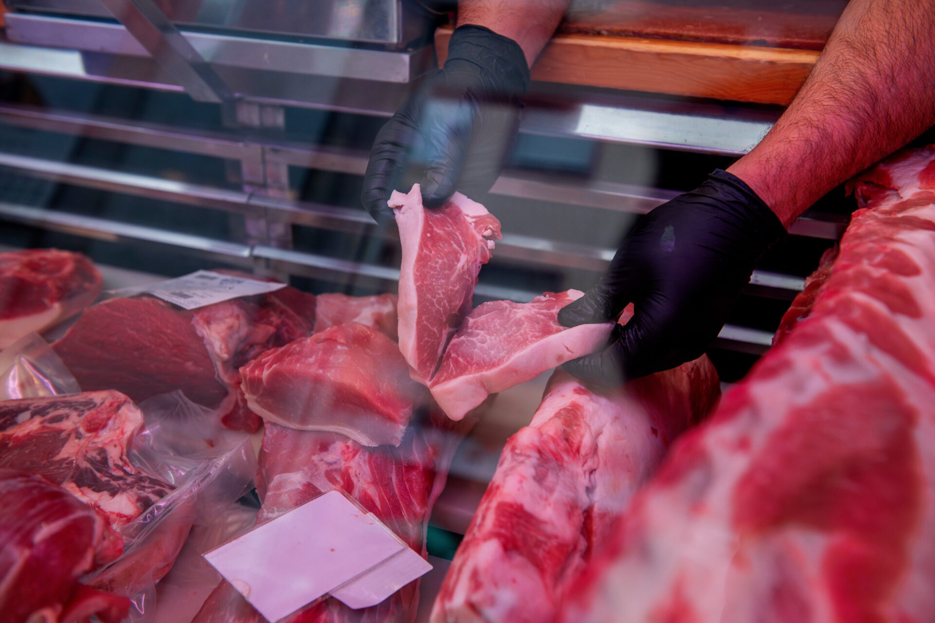 Butcher showing fresh cuts of meat in butcher shop display case